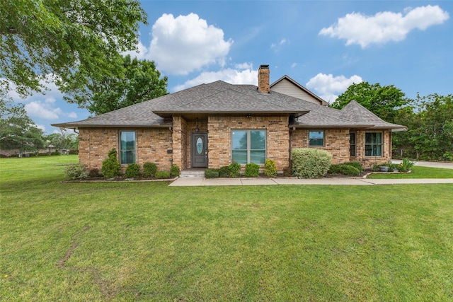 view of front of house with brick siding, a front yard, roof with shingles, and a chimney