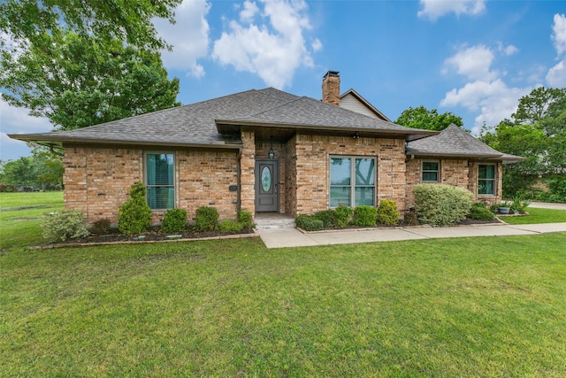 view of front of house featuring a front lawn, a shingled roof, a chimney, and brick siding