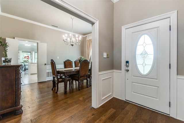 entryway with a chandelier, crown molding, dark wood-type flooring, wainscoting, and a decorative wall