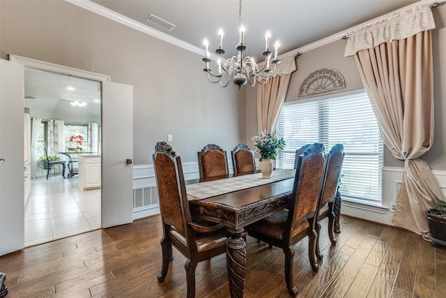 dining space featuring a chandelier, hardwood / wood-style floors, crown molding, healthy amount of natural light, and a wainscoted wall