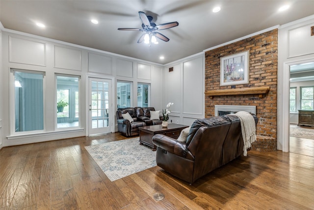 living area with a decorative wall, ornamental molding, a brick fireplace, ceiling fan, and hardwood / wood-style floors