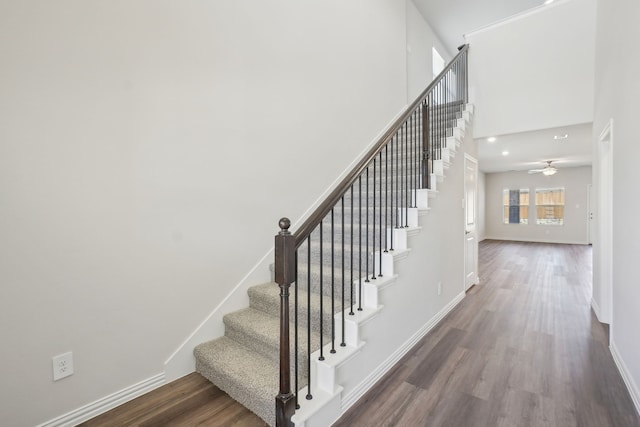 staircase featuring wood finished floors, baseboards, a ceiling fan, and a towering ceiling