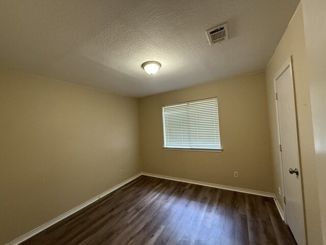 empty room featuring dark wood-style flooring, baseboards, and a textured ceiling