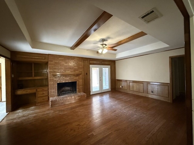unfurnished living room with ceiling fan, a raised ceiling, hardwood / wood-style flooring, a brick fireplace, and a decorative wall
