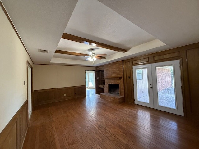 unfurnished living room with a decorative wall, french doors, wood-type flooring, ceiling fan, and beamed ceiling