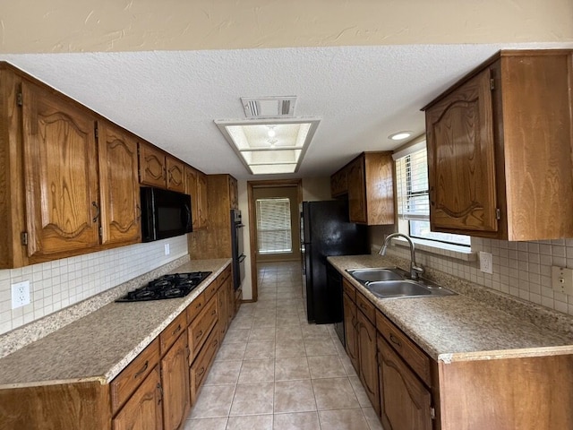 kitchen featuring black appliances, a sink, a textured ceiling, tasteful backsplash, and brown cabinets