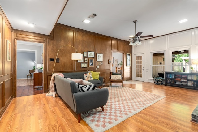 living room with a decorative wall, a ceiling fan, light wood-style floors, french doors, and wood walls