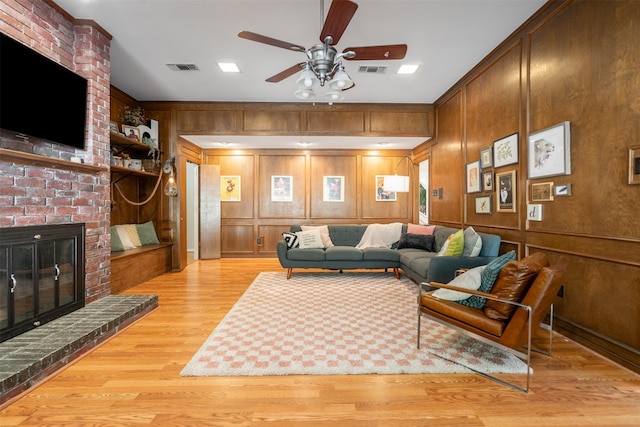 living room with a ceiling fan, light wood finished floors, a fireplace, and wooden walls