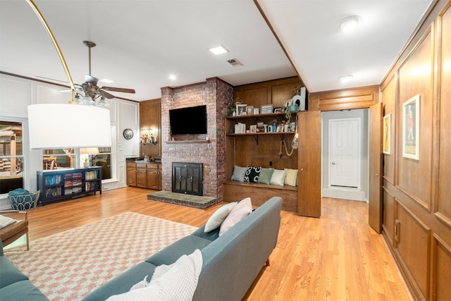living area featuring ceiling fan, a fireplace, light wood-type flooring, and a decorative wall