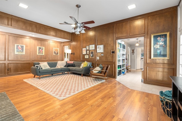 living area with a ceiling fan, light wood-style floors, a decorative wall, ornamental molding, and wooden walls