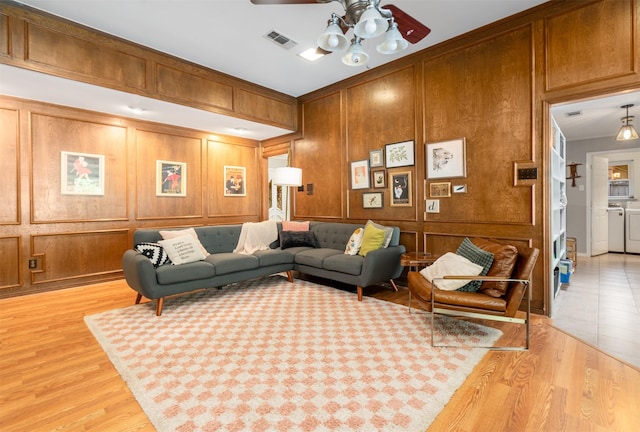 living room featuring a ceiling fan, light wood finished floors, independent washer and dryer, and wooden walls