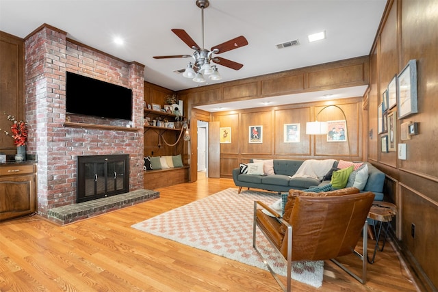 living room with a ceiling fan, wood finished floors, a brick fireplace, and wood walls