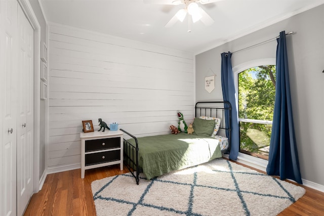 bedroom featuring wood finished floors, wood walls, ceiling fan, and a closet