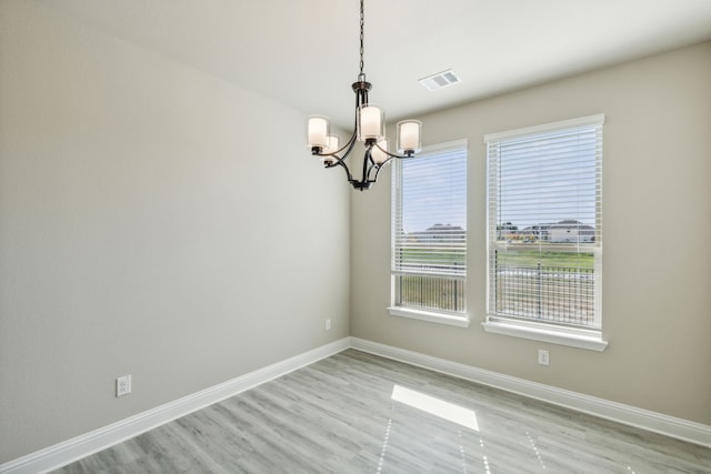 spare room featuring a chandelier, baseboards, and light wood finished floors