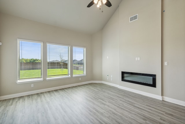 unfurnished living room featuring wood finished floors, ceiling fan, a glass covered fireplace, baseboards, and high vaulted ceiling