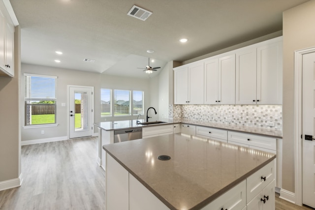 kitchen featuring a sink, stainless steel dishwasher, a peninsula, backsplash, and light wood-style flooring