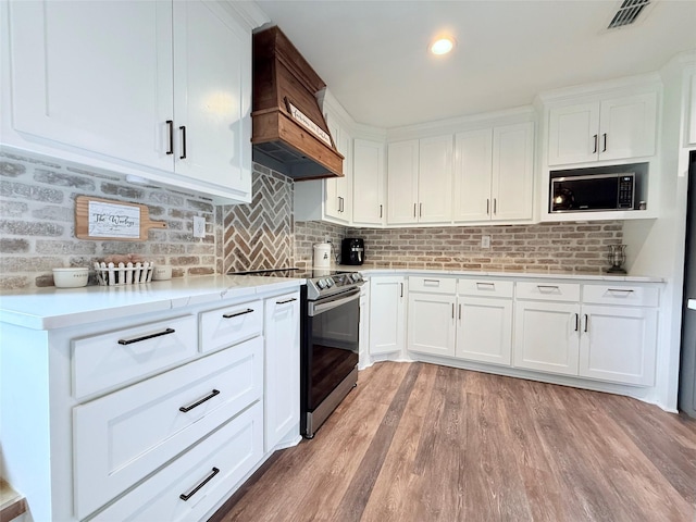 108 Martha Dr, Winnsboro, TX 75494 - kitchen featuring appliances with stainless steel finishes, custom range hood, light wood-type flooring, white cabinetry, and tasteful backsplash