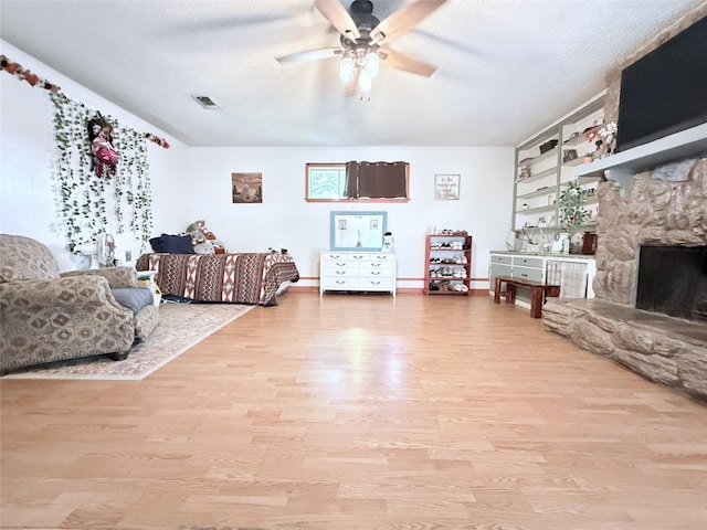 108 Martha Dr, Winnsboro, TX 75494 - living room with a ceiling fan, light wood-style flooring, a textured ceiling, and a stone fireplace