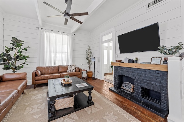 3801 Homan Ave, Waco, TX 76707 - living room featuring beamed ceiling, wood finished floors, a ceiling fan, a fireplace with raised hearth, and wood walls
