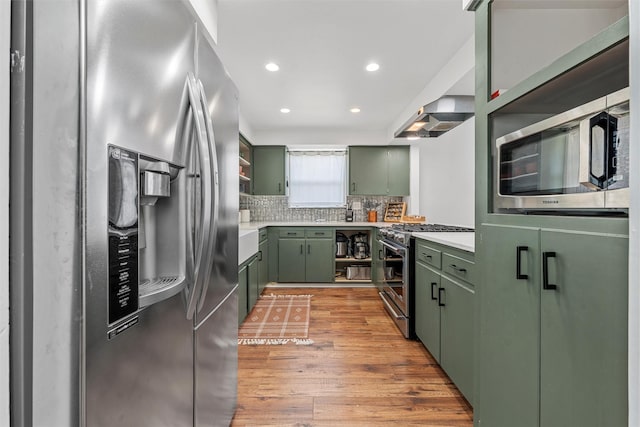 3801 Homan Ave, Waco, TX 76707 - kitchen with green cabinets, stainless steel appliances, wall chimney range hood, light wood-style floors, and light countertops