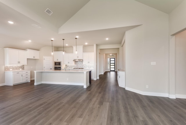 kitchen with vaulted ceiling, stainless steel appliances, a sink, tasteful backsplash, and an island with sink
