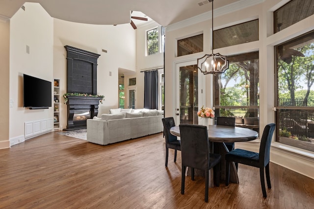 dining space featuring plenty of natural light, wood finished floors, a glass covered fireplace, a chandelier, and a towering ceiling