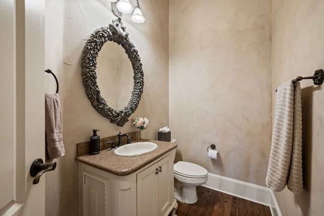 half bath featuring toilet, wood finished floors, vanity, and baseboards