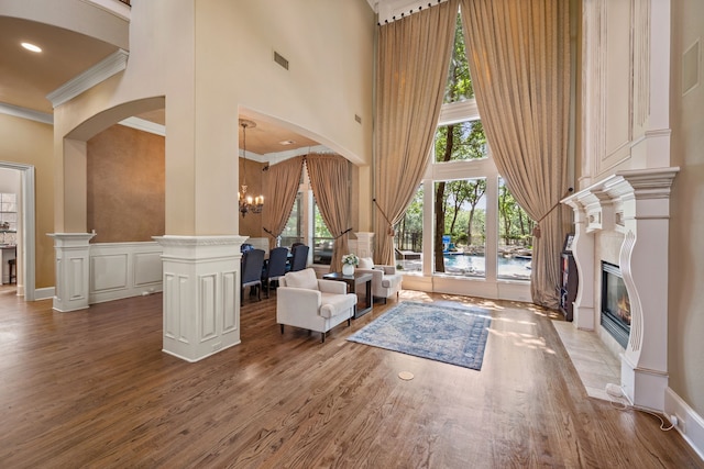 living area featuring a high ceiling, crown molding, wood finished floors, a chandelier, and a fireplace with flush hearth