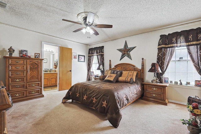 bedroom featuring light colored carpet, a textured ceiling, multiple windows, ensuite bathroom, and ceiling fan