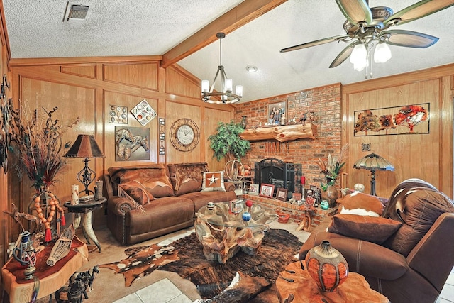 tiled living room featuring a textured ceiling, wooden walls, ceiling fan, a fireplace, and a chandelier