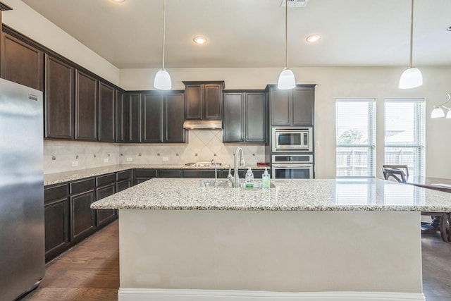 301 Harcourt Ave, Mckinney, TX 75072 - kitchen featuring appliances with stainless steel finishes, a sink, light stone counters, a center island with sink, and dark brown cabinetry