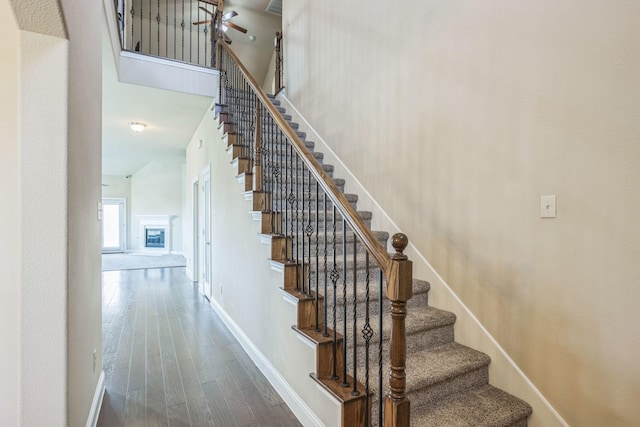 301 Harcourt Ave, Mckinney, TX 75072 - stairs with wood finished floors, baseboards, a ceiling fan, a towering ceiling, and a glass covered fireplace