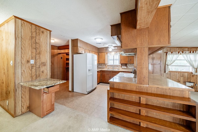 2302 13th, Brownwood, TX 76801 - kitchen featuring white fridge with ice dispenser, a sink, wooden walls, brown cabinets, and a peninsula