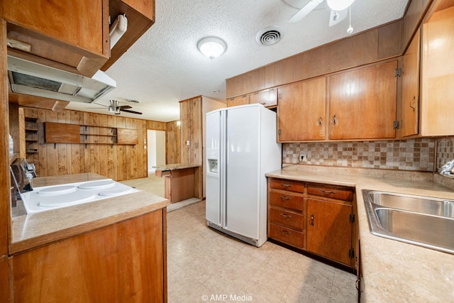 2302 13th, Brownwood, TX 76801 - kitchen featuring a ceiling fan, white refrigerator with ice dispenser, wood walls, a sink, and light countertops