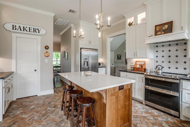 182 Hcr 1431, Covington, TX 76636 - kitchen featuring appliances with stainless steel finishes, a chandelier, tasteful backsplash, a kitchen island, and brick flooring