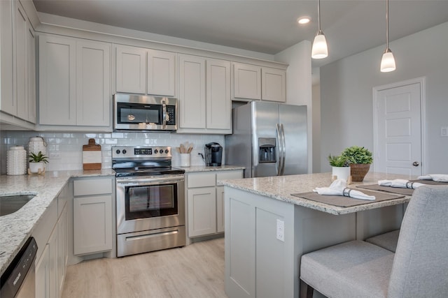 306 Ridge Dr, Justin, TX 76247 - kitchen with appliances with stainless steel finishes, backsplash, a kitchen bar, light wood-type flooring, and light stone countertops