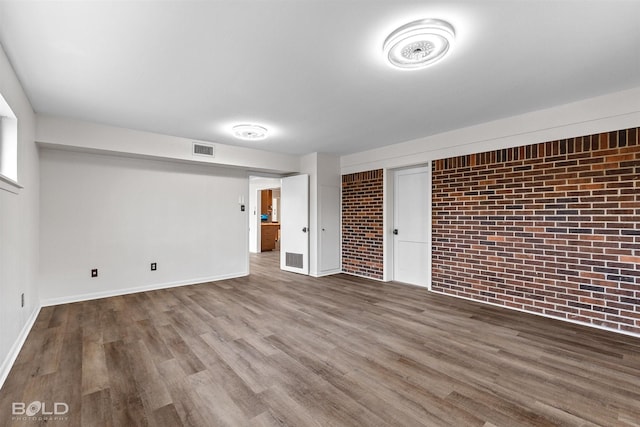 unfurnished living room featuring wood finished floors, baseboards, and brick wall