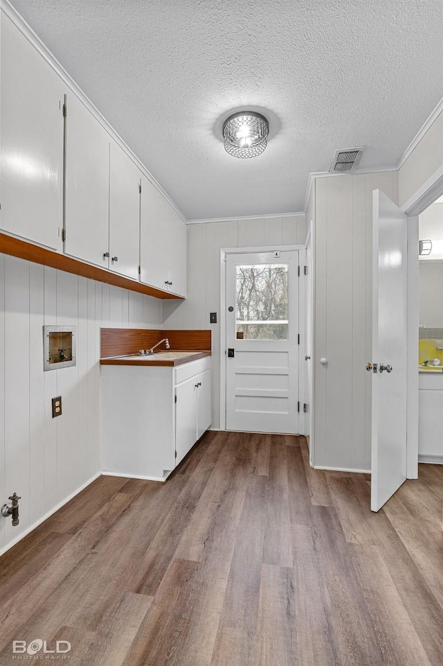 washroom with wood finished floors, a textured ceiling, cabinet space, crown molding, and hookup for a washing machine
