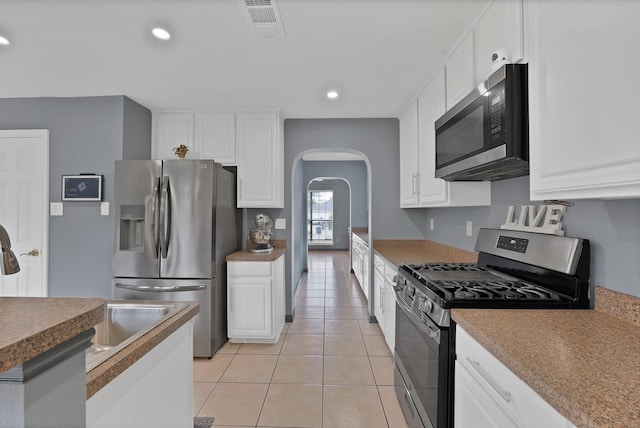kitchen featuring appliances with stainless steel finishes, arched walkways, white cabinetry, light tile patterned floors, and recessed lighting