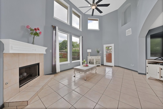 unfurnished living room with a ceiling fan, a high ceiling, a tile fireplace, light tile patterned floors, and arched walkways