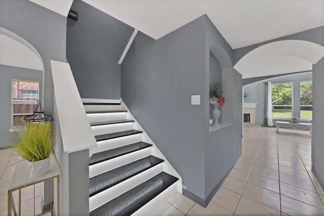staircase featuring arched walkways, tile patterned flooring, a fireplace, and healthy amount of natural light