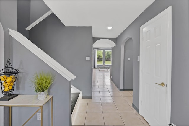 corridor featuring arched walkways, light tile patterned floors, stairs, and baseboards