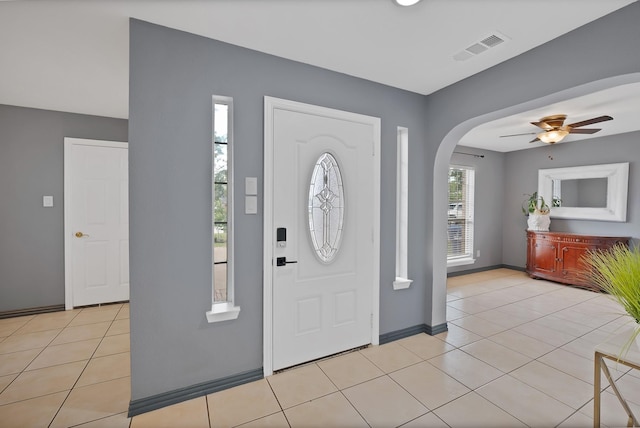 foyer with arched walkways, ceiling fan, light tile patterned flooring, and baseboards