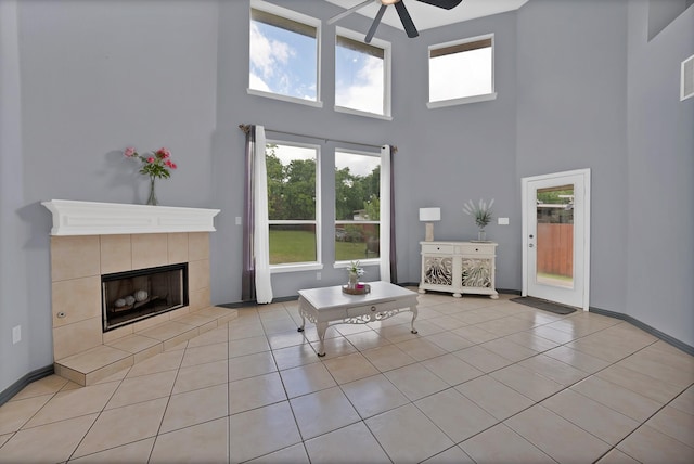 living area with a high ceiling, a ceiling fan, light tile patterned flooring, a tile fireplace, and baseboards