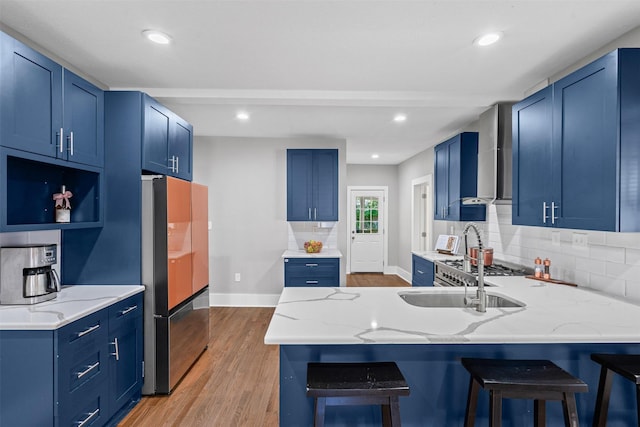 1217 Hawthorne Ave, Fort Worth, TX 76110 - kitchen featuring freestanding refrigerator, a peninsula, blue cabinetry, wall chimney range hood, and light wood finished floors