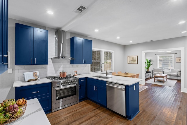 1217 Hawthorne Ave, Fort Worth, TX 76110 - kitchen featuring wall chimney range hood, appliances with stainless steel finishes, a sink, blue cabinets, and recessed lighting