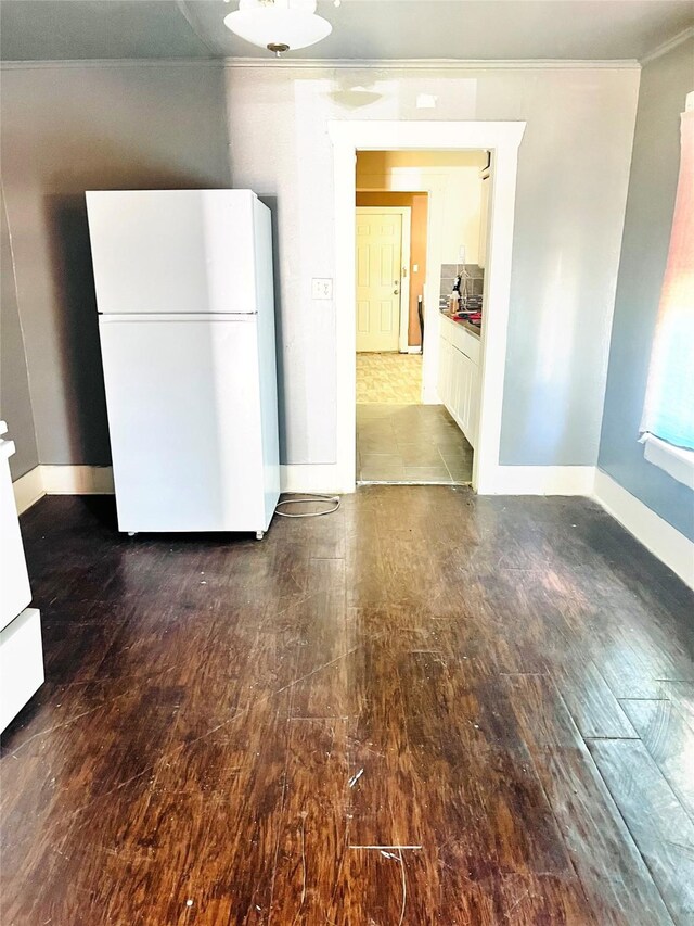 unfurnished dining area featuring dark wood-type flooring, baseboards, and crown molding