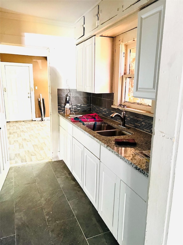 kitchen with a sink, backsplash, white cabinetry, and crown molding