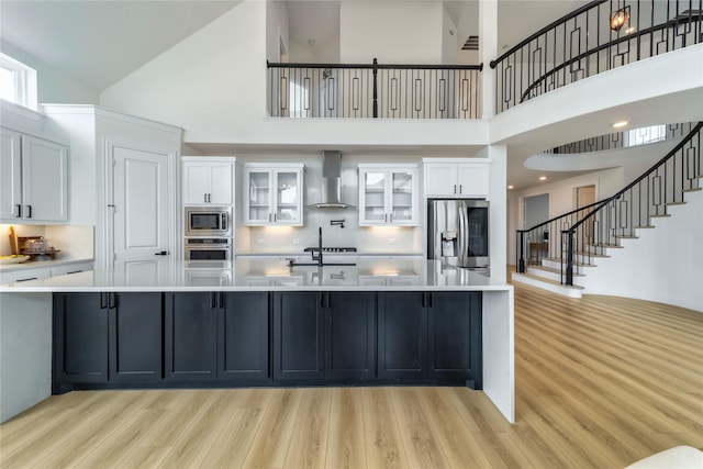 4506 Sky Harbor Dr, Rockwall, TX 75087 - kitchen with appliances with stainless steel finishes, wall chimney range hood, a high ceiling, white cabinets, and light wood-style flooring