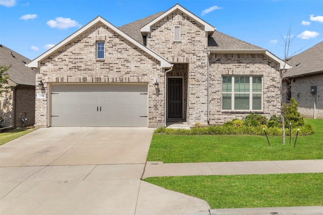 french country inspired facade with a front lawn, brick siding, concrete driveway, roof with shingles, and an attached garage
